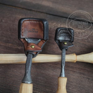 Pu&ograve; includere: Due strumenti per intagliare il legno con manici in pelle. Gli strumenti sono su una superficie di legno. Lo strumento pi&ugrave; grande ha un manico in pelle marrone con il testo "Strongway Tools" in rilievo. Lo strumento pi&ugrave; piccolo ha un manico in pelle nero.