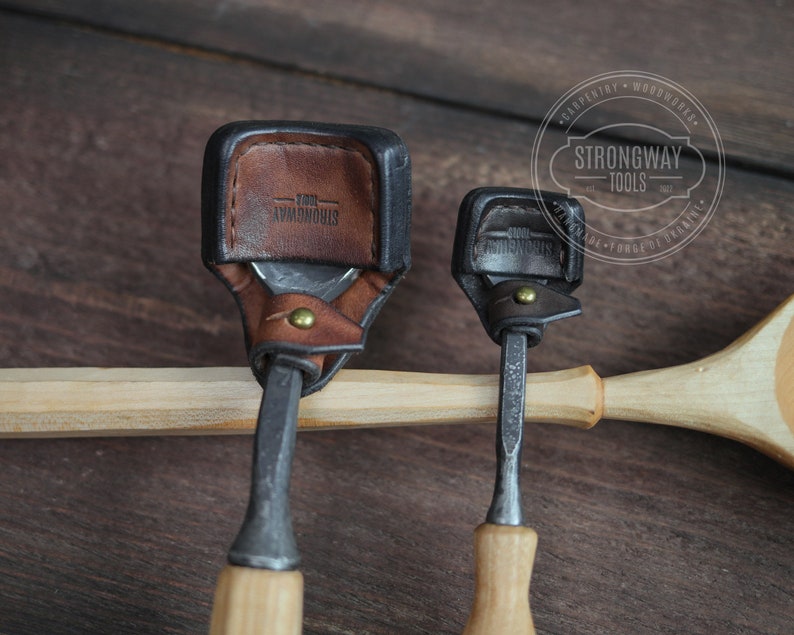 Pu&ograve; includere: Due strumenti per intagliare il legno con manici in pelle. Gli strumenti sono su una superficie di legno. Lo strumento pi&ugrave; grande ha un manico in pelle marrone con il testo "Strongway Tools" in rilievo. Lo strumento pi&ugrave; piccolo ha un manico in pelle nero.