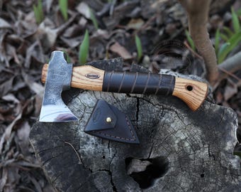 May include: A small, hand-forged axe with a wooden handle wrapped in brown leather. The axe has a polished steel head and a leather sheath.