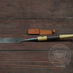 Puede incluir: Un cincel de madera con mango negro y funda de cuero. El cincel está sobre una superficie de madera con un logotipo que dice "Strongway Tools" y "Carpentry Woodworks Handmade Forge of Ukraine".