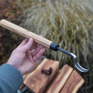 以下が含まれることがあります： 木彫り用の工具で、湾曲した刃が付いています。明るい色の木製のハンドル、黒色のフェルール、湾曲した銀色の刃が特徴です。このツールは、木材の詳細な彫刻と成形のために設計されています。