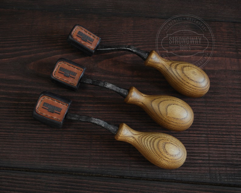 May include: Three wood-handled carving tools with black metal blades. Each tool has a leather label with the text "Strongway Tools" on it.