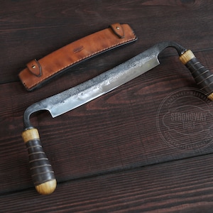 Può includere: Un coltello da intaglio del legno curvo forgiato a mano con un fodero in pelle. Il coltello ha un manico in legno marrone scuro e una lama in metallo con una finitura martellata. Il fodero è in pelle marrone con una cucitura cucita e una chiusura a scatto in metallo. Il coltello è su una superficie in legno scuro.