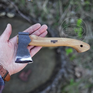 Pode incluir: Um pequeno machado com cabo de madeira e lâmina de metal escuro. O machado é segurado em uma mão, com o texto "STRONGWAY TOOLS" visível no cabo. Projetado para carpintaria e marcenaria.