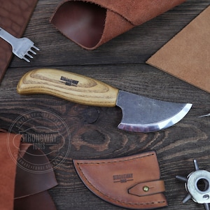 May include: A leatherworking kit with a small knife, a leather punch, a leather awl, and a piece of leather. The knife has a wooden handle and a curved blade. The leather punch has a star-shaped head. The leather awl has a metal handle and a pointed tip. The piece of leather is brown and has a rough texture.