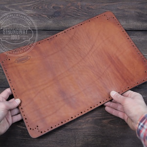 May include: A brown leather piece with holes punched around the edges. The leather is held by two hands. The leather has the text "Strongway Tools" printed on it.