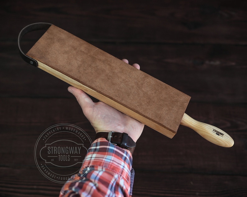 May include: A brown leather strop with a wooden handle. The strop is attached to the handle with a leather strap. The handle has the text "Strongway Tools" printed on it.