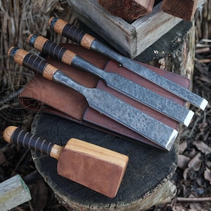 May include: Four wood carving chisels with leather handles and a brown leather roll-up case. The chisels are arranged in a row with the handles facing up. The case is rolled up and tied with a leather strap. The chisels are made of metal and have a hammered finish.