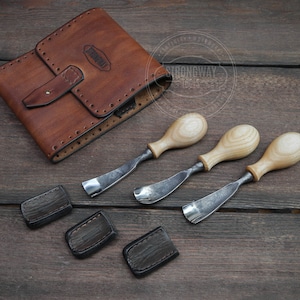 May include: A set of three wood carving tools with wooden handles and metal blades, along with a brown leather case with the text "Strongway Tools" on it. The tools are laid out on a wooden surface.