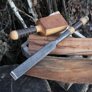 Puede incluir: Un formón para carpintería con un mango de madera envuelto en cuero marrón oscuro y una hoja de metal. También hay un mazo de madera con una superficie de golpeo de cuero. Las herramientas se exhiben sobre bloques de madera, mostrando la artesanía.