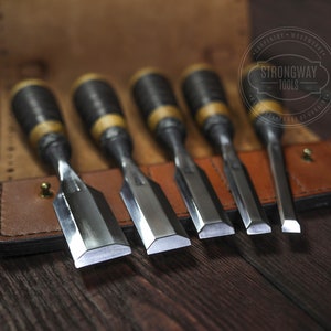 May include: Set of five wood carving chisels with black and brown handles, in a brown leather case. The chisels are arranged in order of size, with the largest chisel at the top and the smallest chisel at the bottom. The case has the text "Strongway Tools" embossed on it.