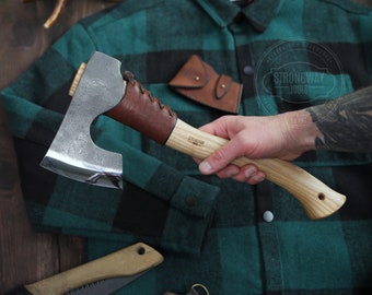 May include: A hand holds a small, hand-forged axe with a brown leather handle and a wooden shaft. The axe has a curved blade and is labeled "Strongway Tools".