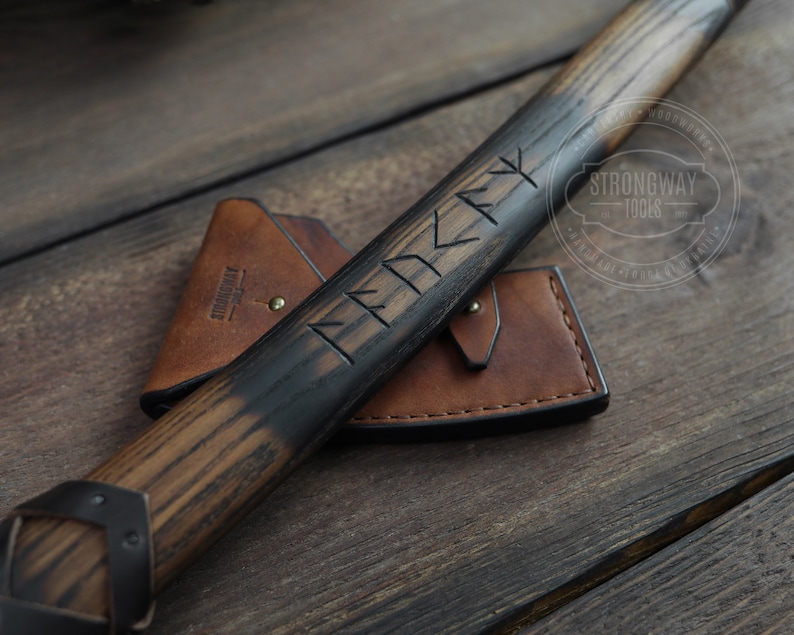 May include: A wooden-handled axe with a black finish and a leather sheath. The handle is engraved with runes and the text "Strongway Tools 1990".