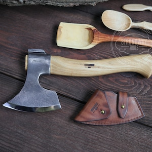 Könnte beinhalten: Eine kleine Axt mit einem Holzstiel und einer Lederscheide. Die Axtkopf ist aus Stahl und hat eine gebogene Klinge. Der Stiel ist mit den Worten "Strongway Tools" gekennzeichnet.