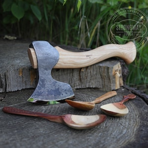 以下が含まれることがあります： 木製の柄と黒く焼かれた鋼鉄製のヘッドを持つ手打ちの斧。斧は木の切り株の上に置かれ、その横に3本の木製のスプーンが置かれている。斧のヘッドには「Strongway Tools」という文字が刻印されている。