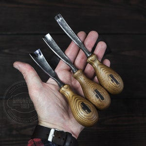 May include: Three wood carving tools with wooden handles. The tools have different shaped blades and are labeled "Strongwood Tools".