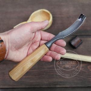 May include: A wood carving tool with a curved blade and a wooden handle. The tool is held in a hand and the brand "Strongway Tools" is visible in the background.