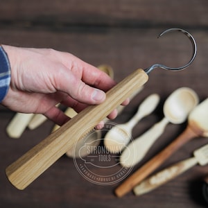 May include: A wooden handled carving tool with a curved metal hook. The tool is held in a hand, and there are other wooden tools in the background. The tool is labelled "Strongway Tools - Handmade - Forge of Ukraine".