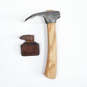 Puede incluir: Una herramienta de talla con mango de madera curvado, una cuchilla de metal y una funda de cuero marrón.