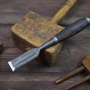 以下が含まれることがあります： 木製の柄と金属製の刃を持つ木工用のみのクローズアップ。のみは木製のブロックの上に置かれています。