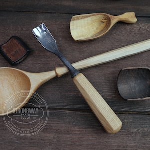 May include: A collection of handcrafted wooden carving tools, including a gouge with a metal blade and wooden handle, and various wooden spoons and scoops. The tools are arranged on a dark wooden surface. The logo "STRONGWAY TOOLS" is visible.