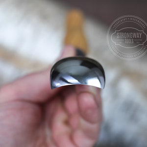 May include: Close-up of a silver-colored woodworking tool with a rounded edge. The tool is held in a hand. The brand name "Strongway Tools" is visible in the background.