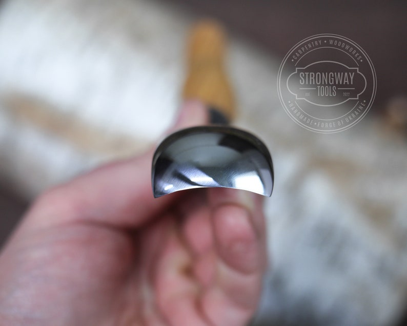 May include: Close-up of a silver-colored woodworking tool with a rounded edge. The tool is held in a hand. The brand name "Strongway Tools" is visible in the background.
