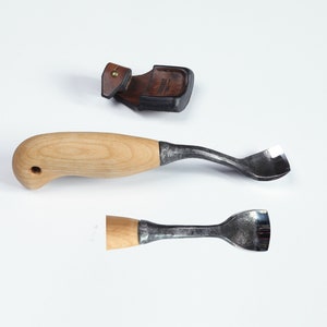 May include: Two wood carving tools with wooden handles and metal blades. The tools are on a white surface. One tool has a curved blade and the other has a straight blade.