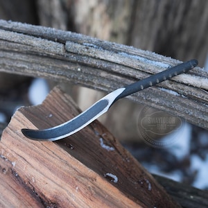 Puede incluir: Un cuchillo curvo negro y plateado con mango de madera. El cuchillo está apoyado en una pieza de madera con una superficie desgastada. El texto "Swaylobor Tools" es visible en el fondo.