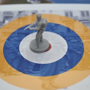 May include: A grey plastic miniature soldier figure holding a rifle, standing on a white, blue and yellow target.