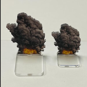 Peut inclure: Deux miniatures d'explosion en acrylique. Les miniatures présentent un nuage de fumée gris foncé avec une base de flamme jaune et orange, montées sur des socles rectangulaires transparents. Conçues pour les jeux de table.