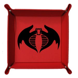 May include: A red, square tray with a black cobra logo in the center. The tray has a stitched border and rounded corners with snaps. The cobra logo features a stylized cobra head with wings and a series of horizontal lines.