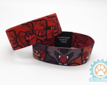 May include: Two red and black woven wristbands with a cartoon wolf design. The wristbands have the text "Furnique Merch .com" printed on them.
