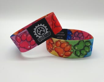 May include: Two colorful woven wristbands with a paw print design. The top wristband has a black patch with a gear and paw print logo and the text "Craftier Workshop".