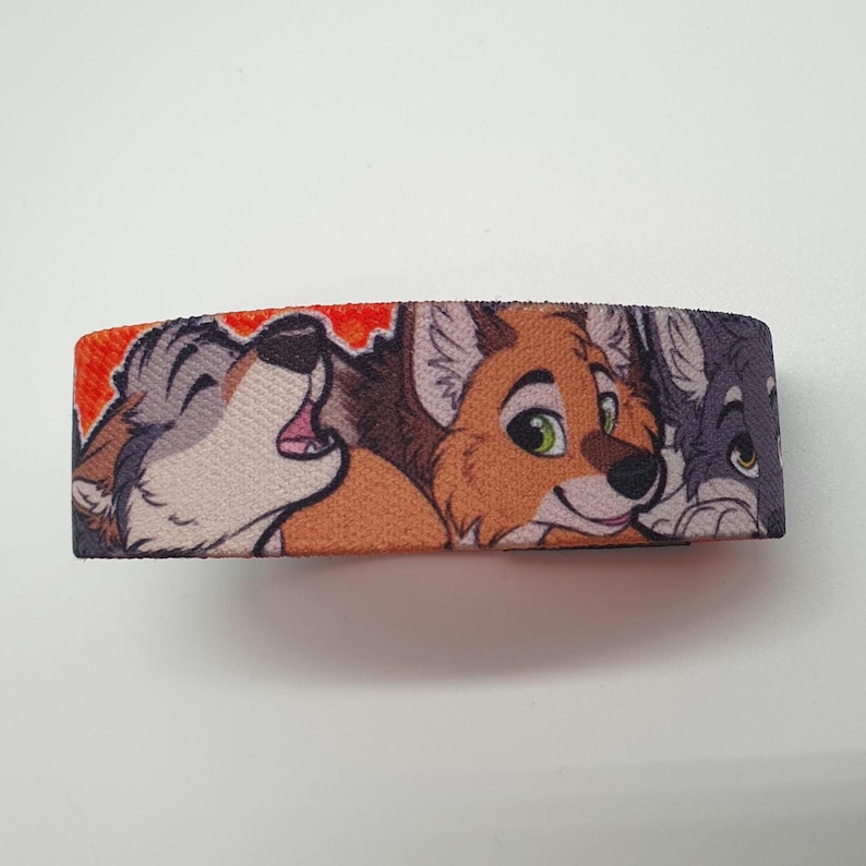 May include: A colorful wristband with a design featuring three cartoon animal faces. The animals are a wolf, a fox, and a dog. The wolf is howling and the fox is smiling. The wristband is made of a soft, comfortable material.