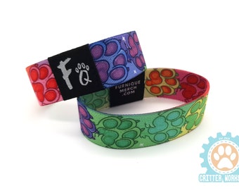 May include: Two colorful woven wristbands with a paw print design. The wristbands are layered on top of each other. The top wristband has a black tag with the text "FURNIQUE MERCH .COM". The bottom wristband has a black tag with the text "FQ".
