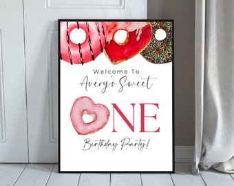 Könnte beinhalten: Willkommen zu Averys Sweet One Geburtstagsparty! Ein druckbares Schild mit Donut-Motiv mit drei Donuts mit rosa, rotem und braunem Zuckerguss. Die Donuts sind mit Streuseln und Schokolade verziert.