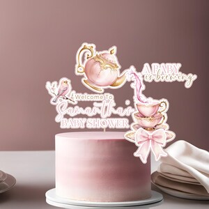 Op de afbeelding: Een roze en gouden theepot en theekopje caketopper met een roze strik en de tekst "A baby is brewing" en "Welcome to Samantha's Baby Shower".