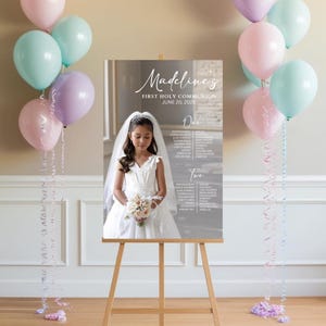 May include: A gray and white poster with a photo of a young girl in a white dress and veil. The poster says "Madeline's First Holy Communion June 20, 2023" and has a seating chart.