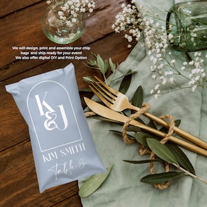 May include: A light blue favor bag with a white arch design and the initials "K & J" in a white script font. The bag also has the text "KIM SMITH Table 8" in white.