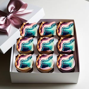 May include: A box of nine cupcakes decorated with colorful agate-inspired designs and the text "Pamela Anderson's Bridal Shower" on each cupcake.