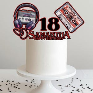 Könnte beinhalten: Eine weiße Torte auf einem weißen Kuchenständer, verziert mit einem Aufsatz mit einer Kassette, Kopfhörern und der Zahl 18. Der Aufsatz enthält auch den Namen "Samantha" und "Happy Birthday."
