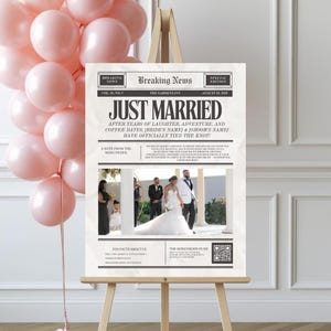 May include: A wedding sign on an easel with the headline "JUST MARRIED" in bold, black letters. The sign resembles a newspaper, with the text "Breaking News" at the top and a photo of the couple. Pink balloons are in the background.