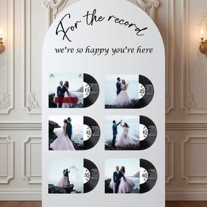 May include: White wedding sign with the text "For the record, we're so happy you're here." Six black vinyl record designs feature wedding photos. The sign is arched at the top and set against a white wall.