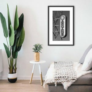 A black and white photograph of a vintage arcade sign on the Wildwood, NJ Boardwalk hangs on a wall next to a futon sofa.