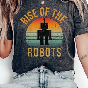 May include: A dark gray t-shirt with a vintage-style graphic of a robot in front of a sunset. The text "Rise of the Robots" is printed in yellow on the shirt.