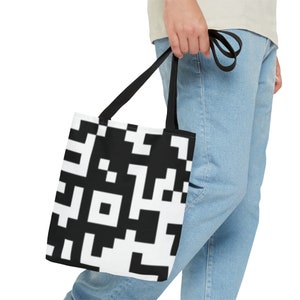 Könnte beinhalten: Eine schwarz-weiße Einkaufstasche mit einem QR-Code-Muster. Die Tasche hat schwarze Henkel und wird von einer Person gehalten.
