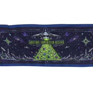 Könnte beinhalten: Eine rechteckige Webdecke mit einer dunkelblauen Weltraumszene, in der ein silbernes UFO ein hellgrünes Licht in Form eines Weihnachtsbaums nach unten strahlt. Der Text CHRISTMAS TRANSMISSION RECEIVED steht in Gelb über dem Lichtstrahl.