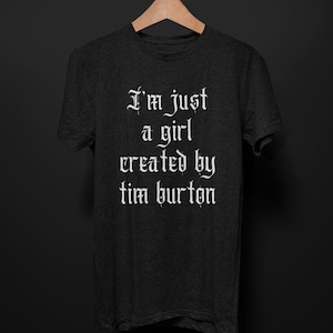 May include: A dark gray t-shirt with the text "I'm just a girl created by tim burton" in white gothic font.