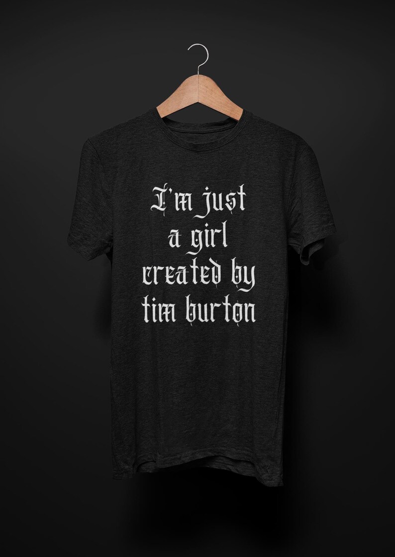 May include: A dark gray t-shirt with the text "I'm just a girl created by tim burton" in white gothic font.